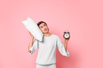 Overslept young woman with pillow and alarm clock on pink background