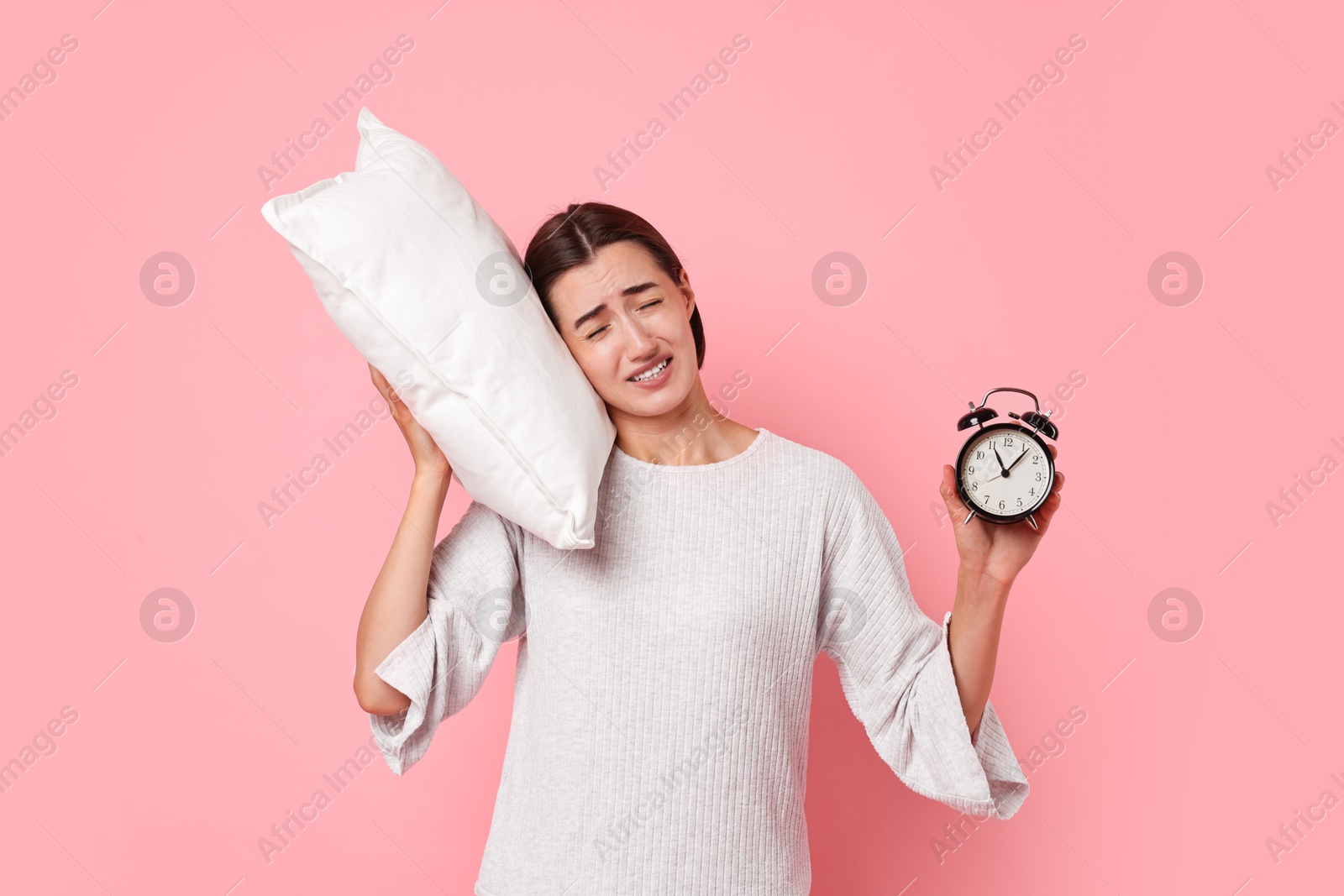 Photo of Overslept young woman with pillow and alarm clock on pink background