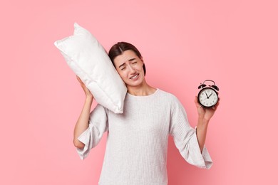 Overslept young woman with pillow and alarm clock on pink background