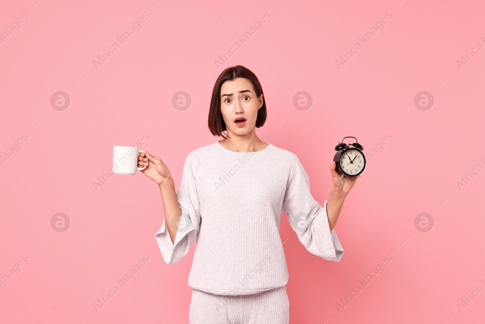 Photo of Overslept young woman with cup and alarm clock on pink background