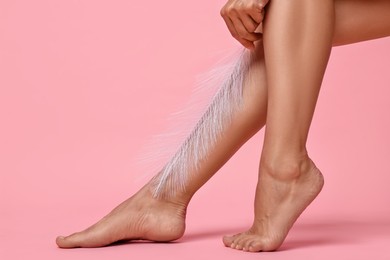 Photo of Woman with smooth legs and feather on pink background, closeup