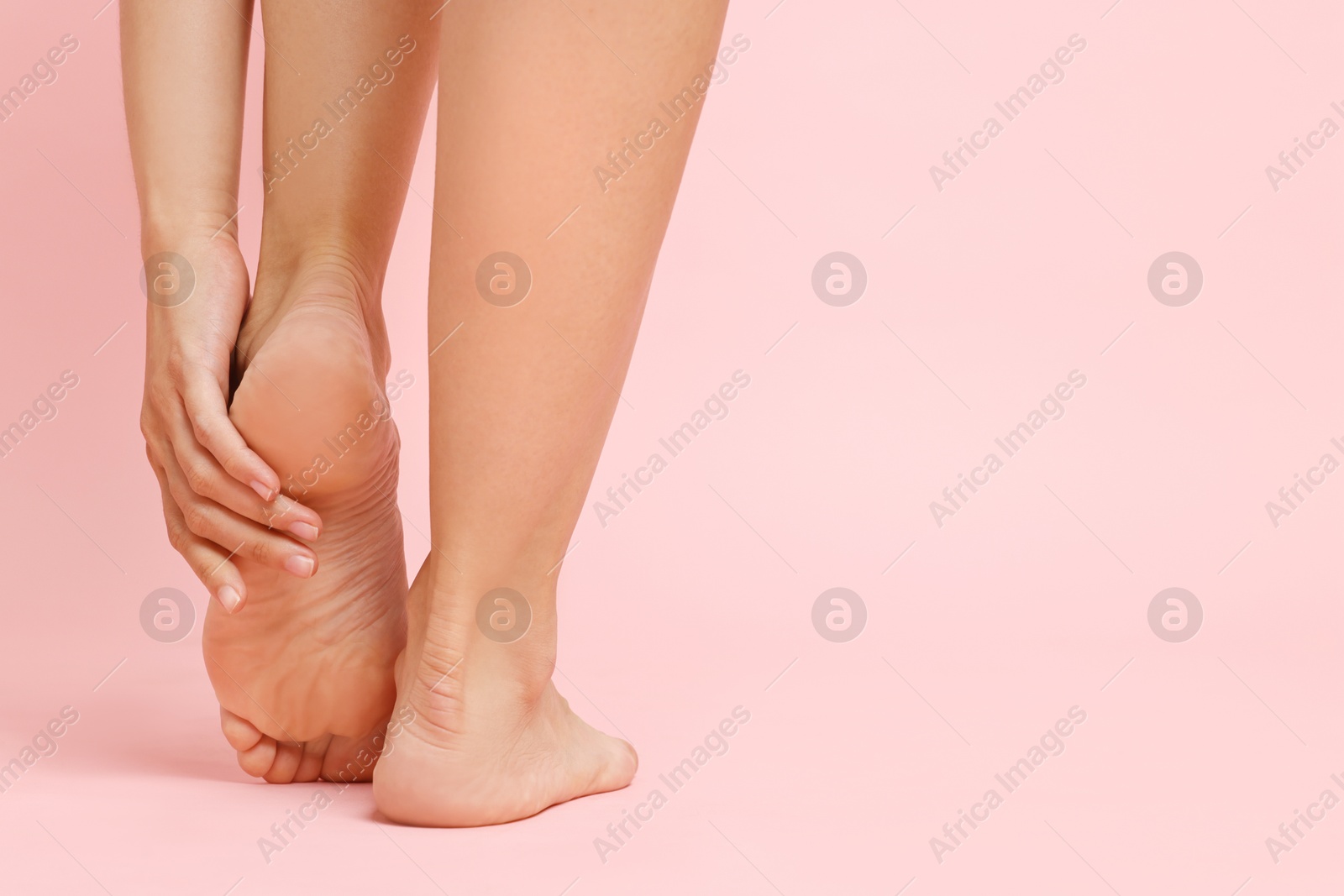 Photo of Woman touching her smooth feet on pink background, closeup. Space for text