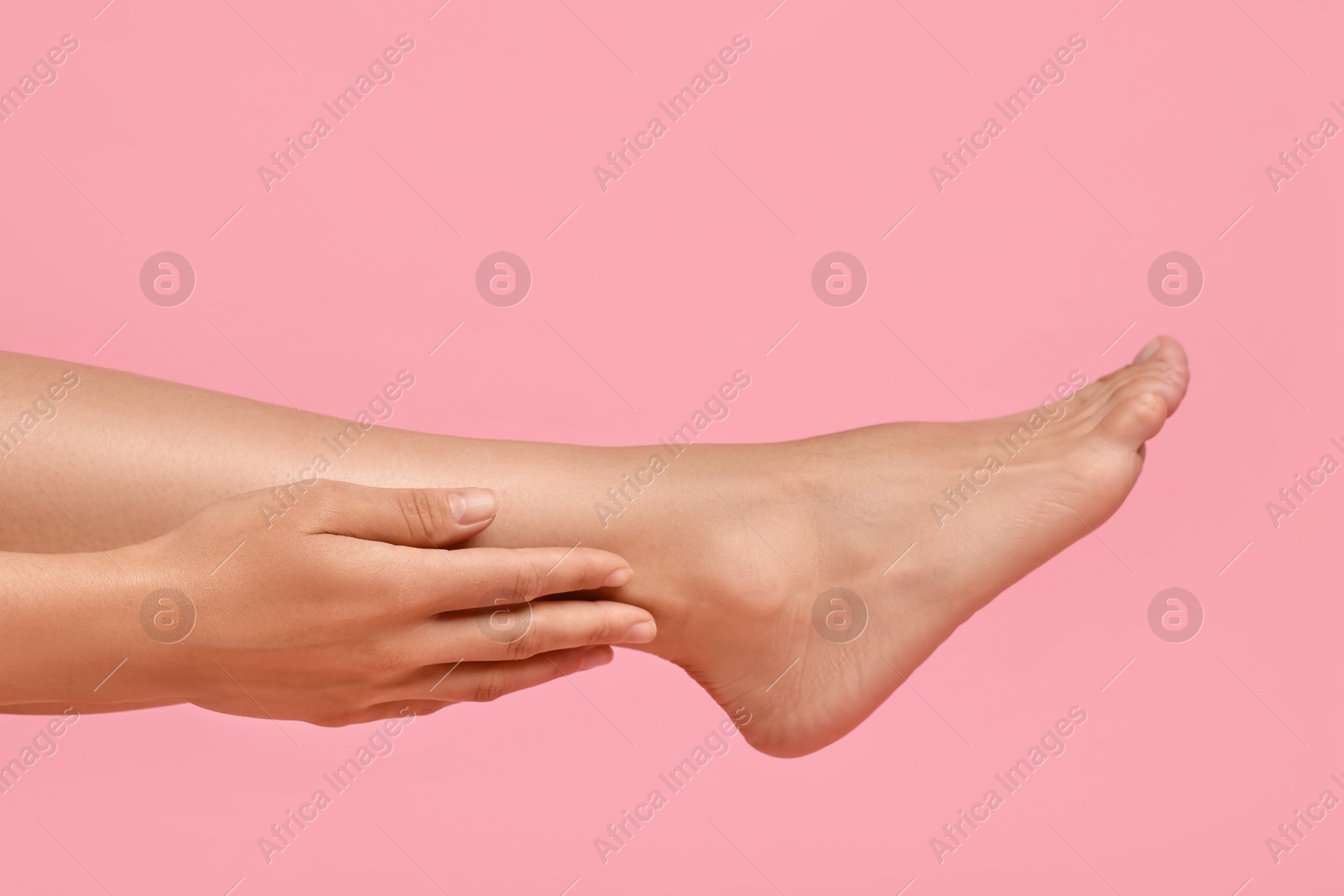 Photo of Woman touching her smooth feet on pink background, closeup