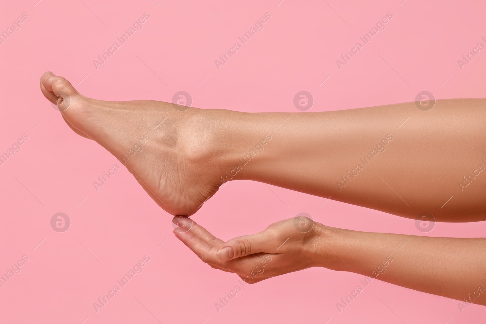 Photo of Woman touching her smooth feet on pink background, closeup