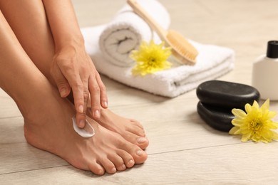 Photo of Woman applying moisturizing cream onto her feet on floor, closeup. Body care