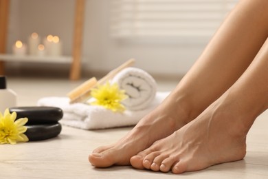 Photo of Woman with smooth feet, flowers and spa supplies on floor, closeup. Body care