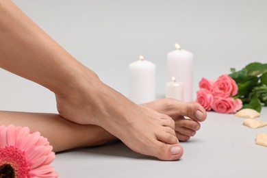 Photo of Woman with smooth feet, burning candles, petals and flowers on grey background, closeup