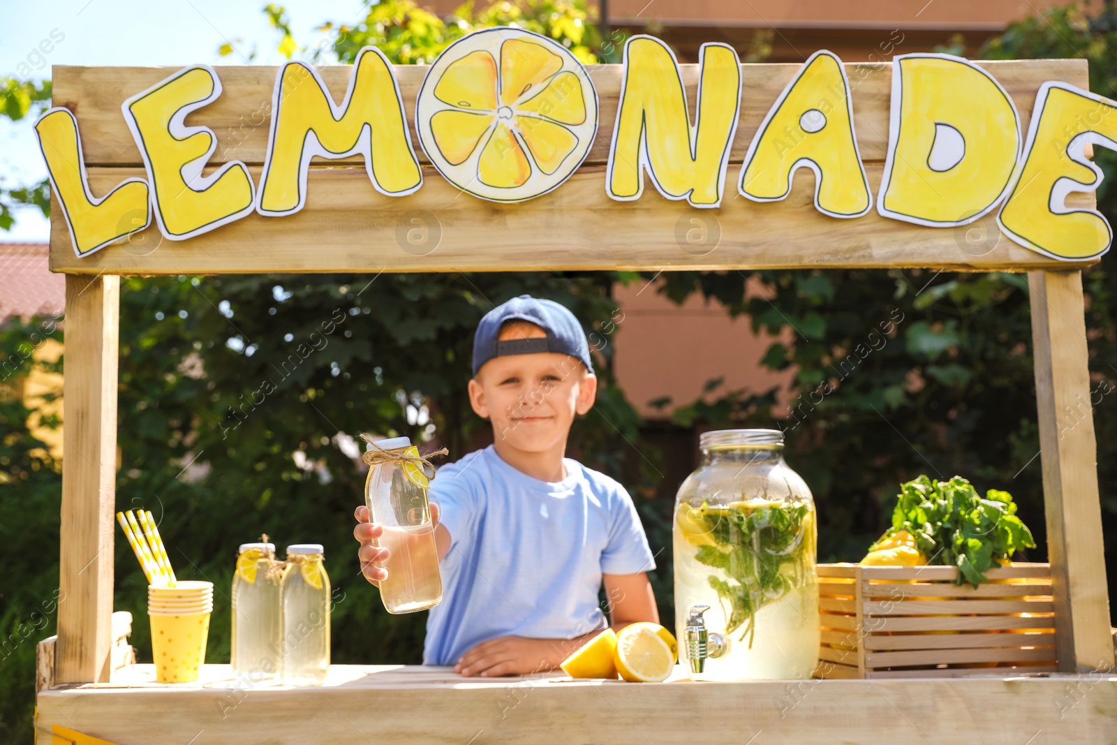 Photo of Cute little boy with refreshing drink at lemonade stand in park