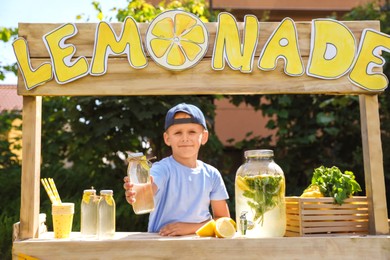 Photo of Cute little boy with refreshing drink at lemonade stand in park