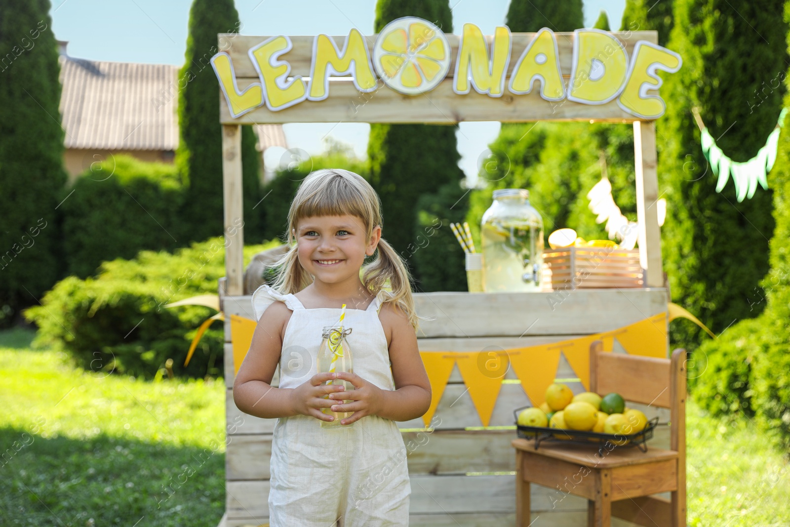 Photo of Cute little girl with refreshing drink near lemonade stand in park