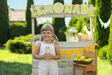 Cute little girl with refreshing drink near lemonade stand in park