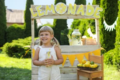 Photo of Cute little girl with refreshing drink near lemonade stand in park