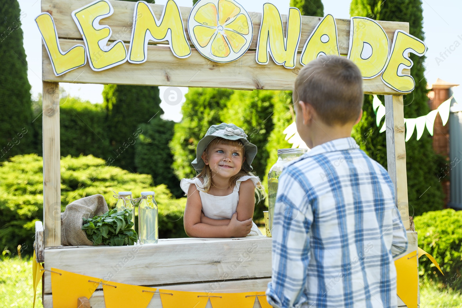 Photo of Cute little girl selling natural lemonade to boy in park