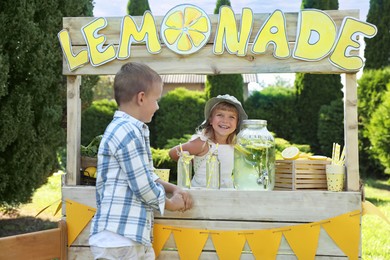 Cute little girl selling natural lemonade to boy in park