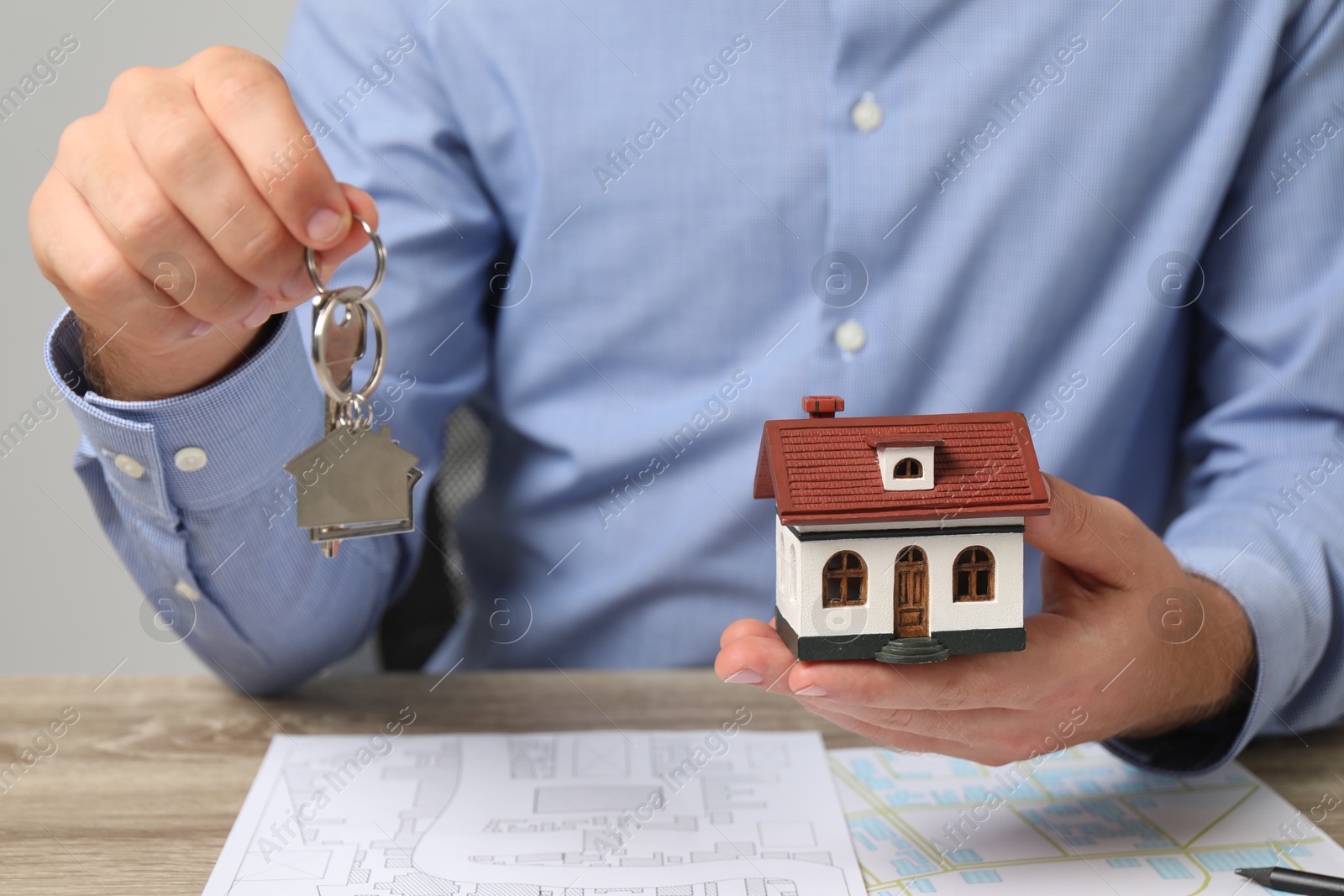 Photo of Real estate agent with key and house model at wooden table, closeup