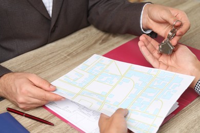 Photo of Real estate agent giving house key to new owner at wooden table, closeup