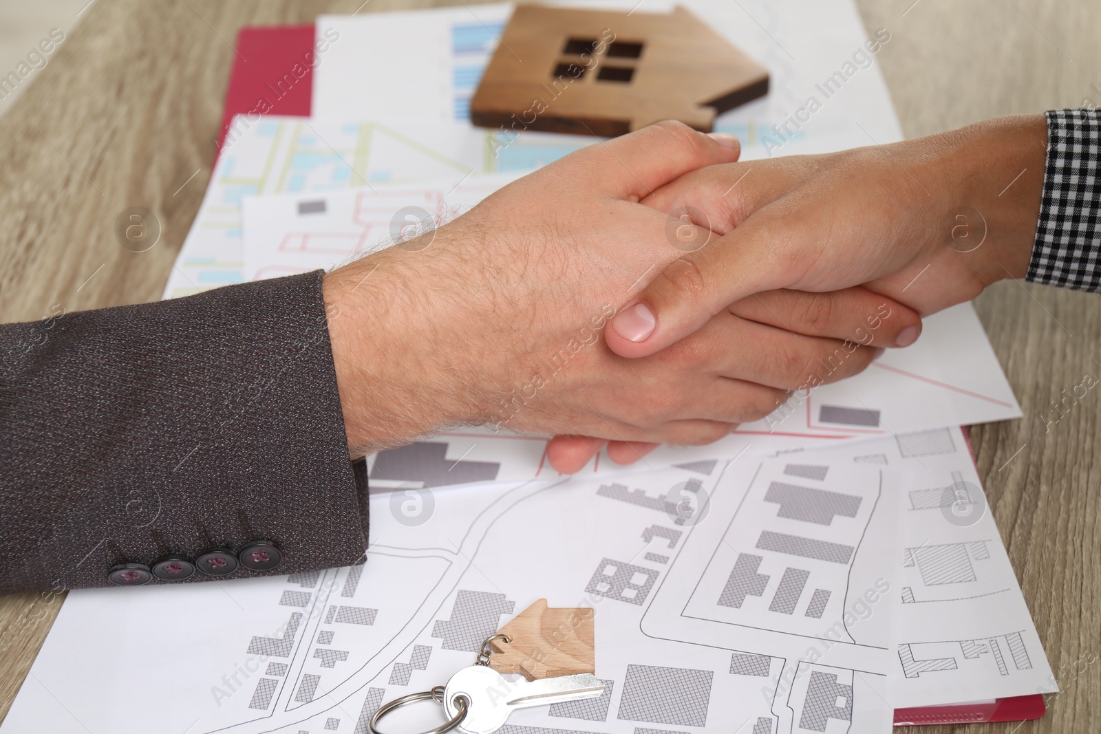 Photo of Real estate agent shaking hands with client at wooden table, closeup