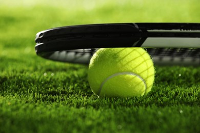 Photo of Tennis racket and ball on green grass, closeup