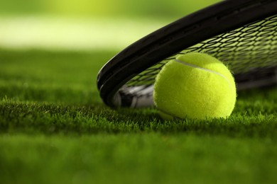 Photo of Tennis racket and ball on green grass, closeup. Space for text