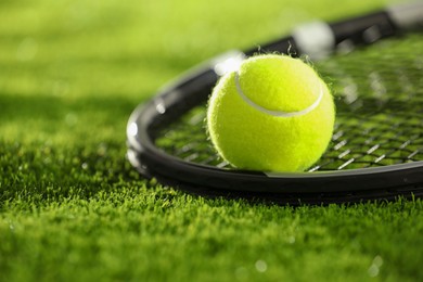 Photo of Tennis racket and ball on green grass, closeup. Space for text