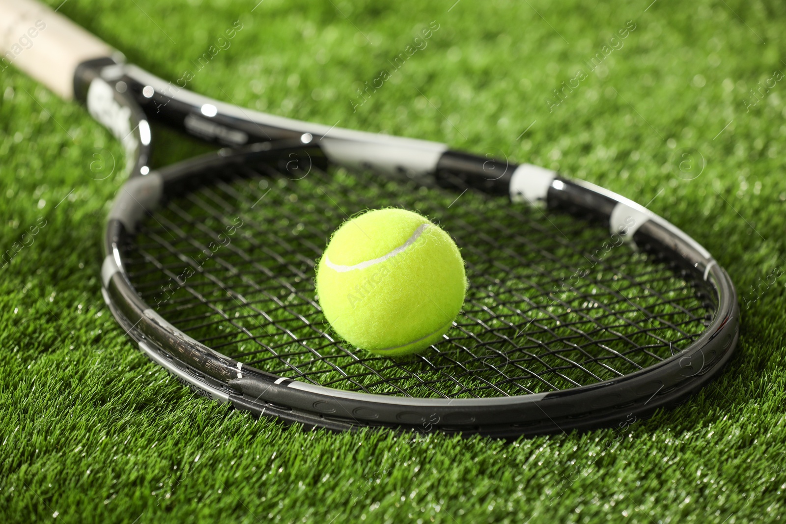 Photo of Tennis racket and ball on green grass, closeup