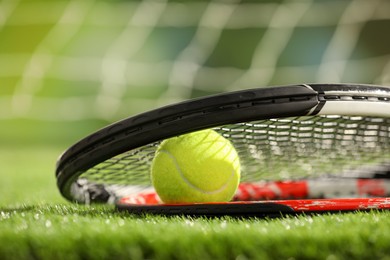 Photo of Tennis racket and ball on green artificial grass, closeup