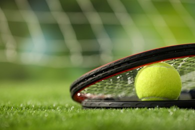 Photo of Tennis racket and ball on green artificial grass, closeup