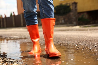 Photo of Woman wearing orange rubber boots standing in puddle outdoors, closeup