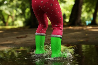 Little girl wearing green rubber boots standing in puddle outdoors, closeup