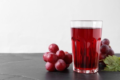 Photo of Tasty grape juice in glass and berries on dark textured table against light background, closeup. Space for text