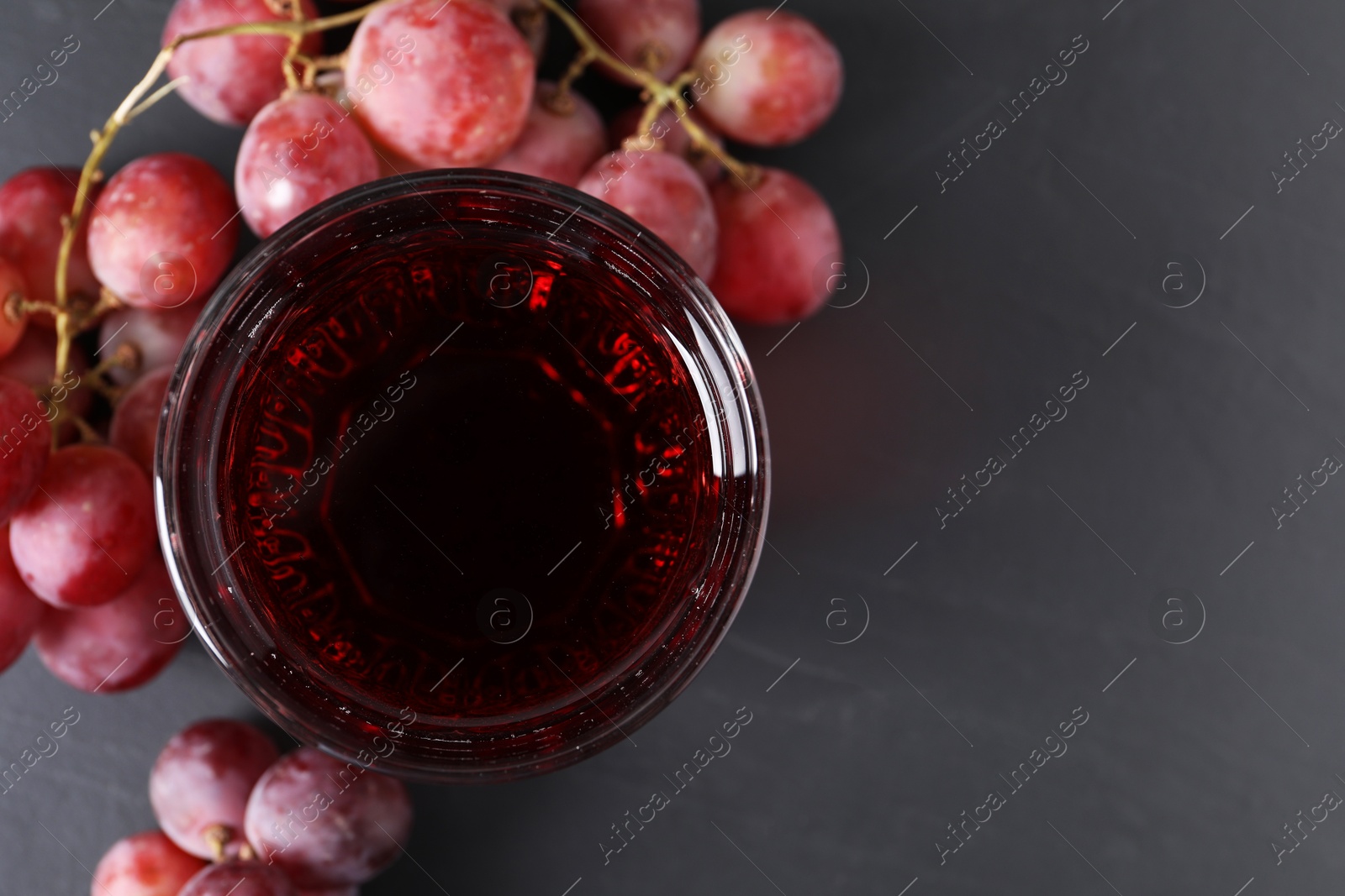 Photo of Tasty grape juice in glass and berries on dark textured table, flat lay. Space for text