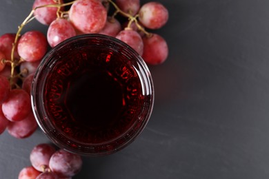 Photo of Tasty grape juice in glass and berries on dark textured table, flat lay. Space for text