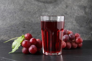 Tasty grape juice in glass, leaf and berries on dark textured table, closeup