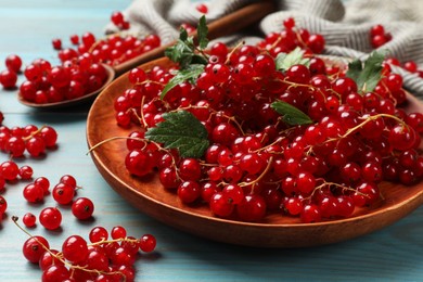 Photo of Fresh red currants and leaves on light blue wooden table, closeup