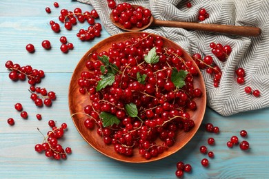 Photo of Fresh red currants and leaves on light blue wooden table, flat lay