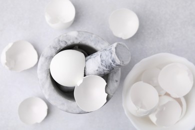 Photo of Broken eggshells, mortar and pestle on grey table, flat lay