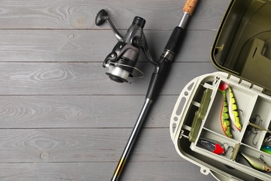 Different fishing tackles in box and rod with spinning reel on grey wooden table, top view. Space for text