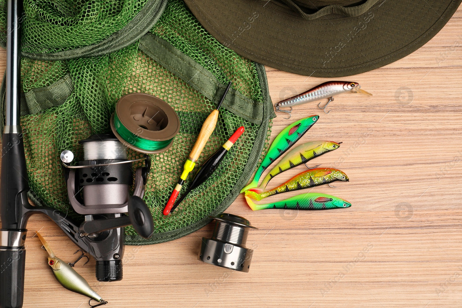 Photo of Fishing rod with spinning reel, baits, hat, net, floats and line on wooden table, top view