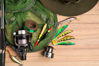 Photo of Fishing rod with spinning reel, baits, hat, net, floats and line on wooden table, top view