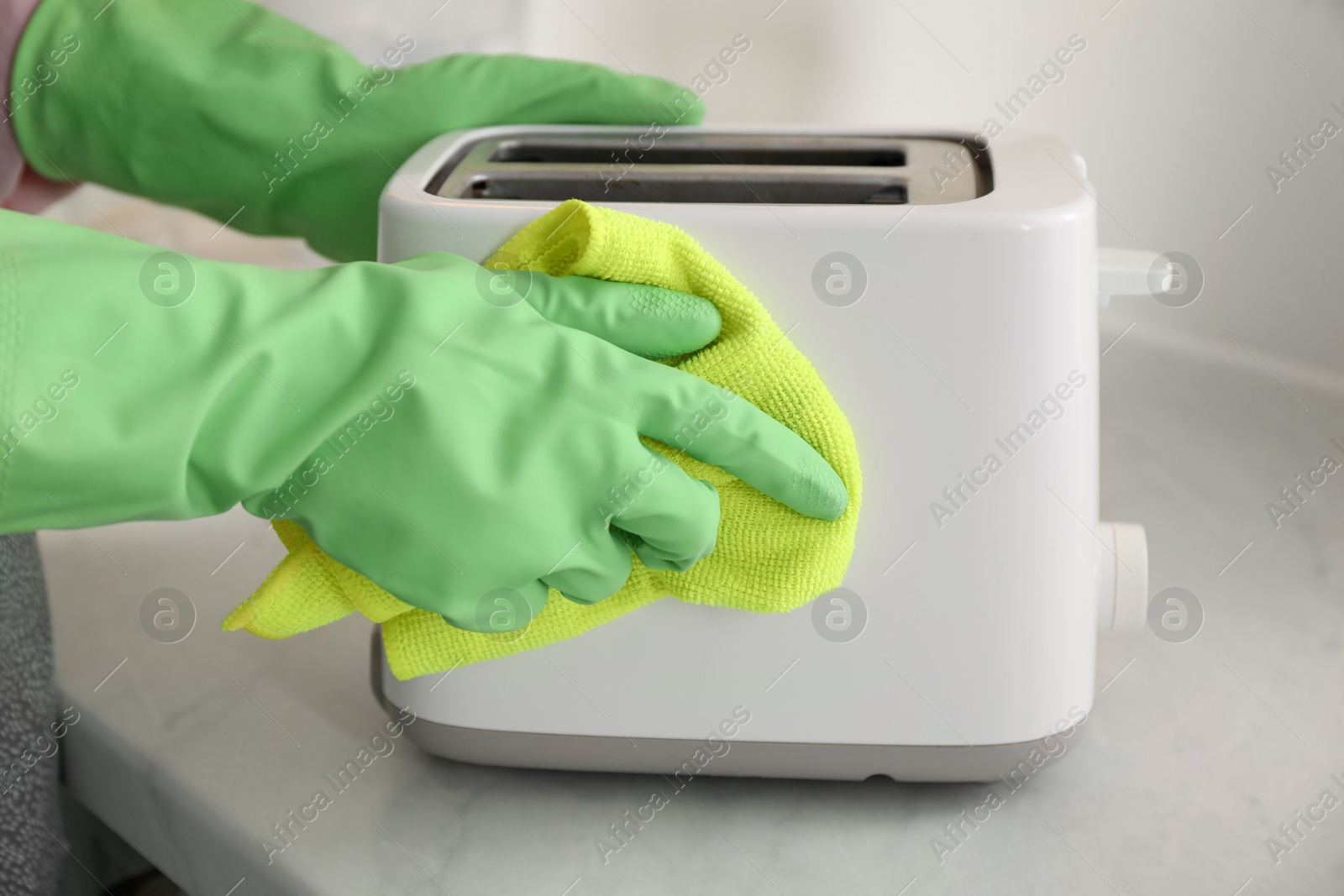 Photo of Woman wiping toaster with rag at countertop in kitchen, closeup