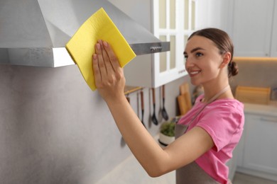 Beautiful young woman cleaning kitchen hood with napkin at home, selective focus