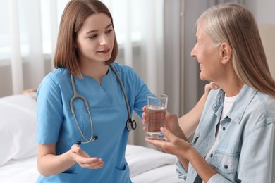 Young healthcare worker consulting senior patient on bed indoors