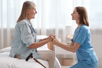 Photo of Smiling healthcare worker supporting senior patient indoors