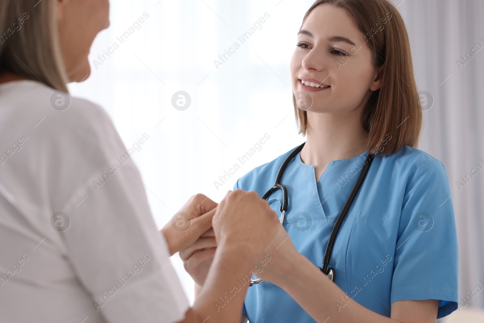 Photo of Smiling healthcare worker in uniform supporting patient indoors, closeup