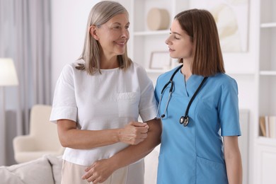 Photo of Young healthcare worker supporting senior patient indoors