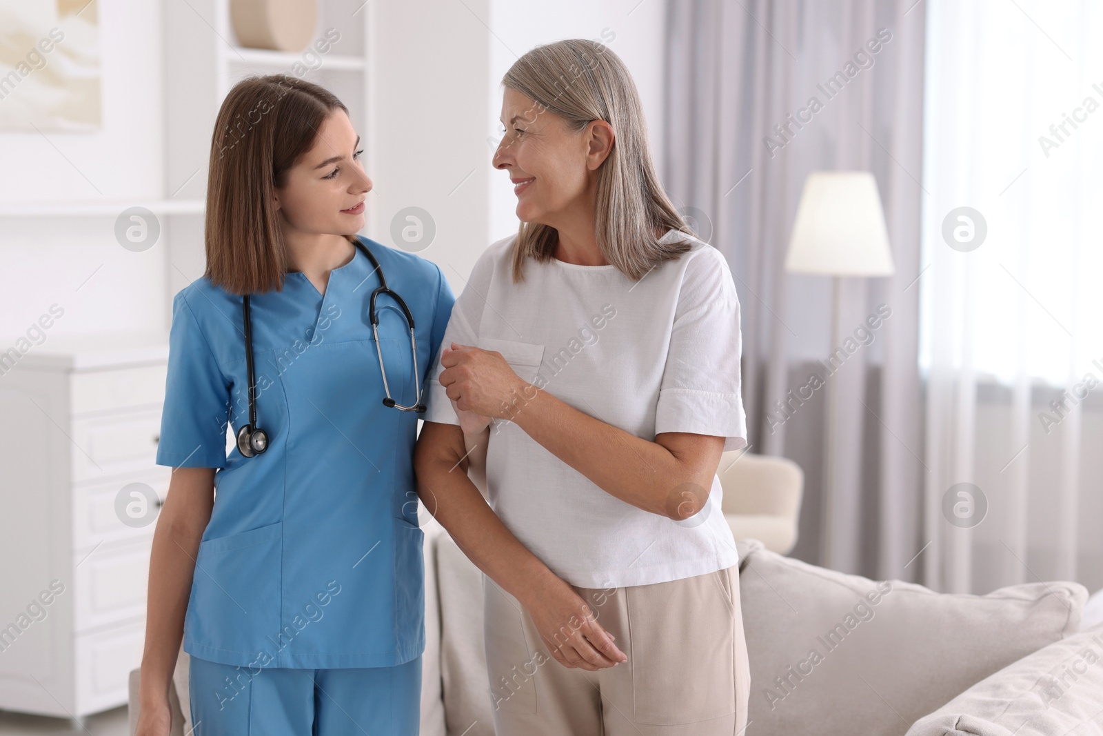 Photo of Young healthcare worker supporting senior patient indoors. Space for text