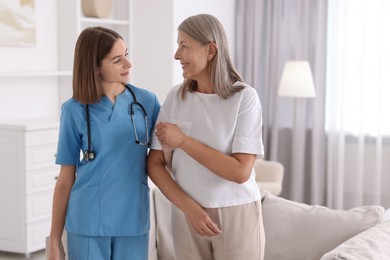 Photo of Young healthcare worker supporting senior patient indoors. Space for text