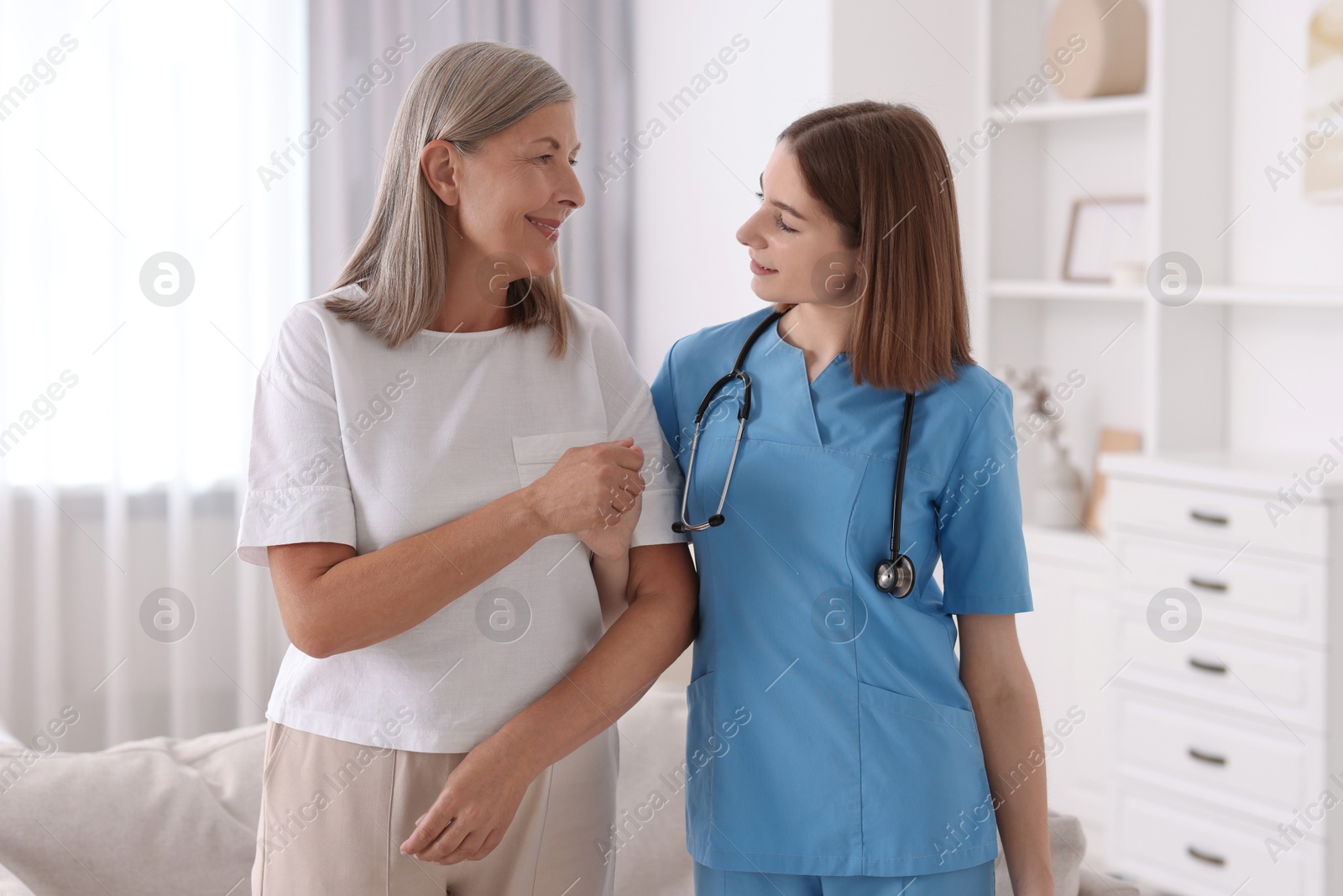 Photo of Young healthcare worker supporting senior patient indoors