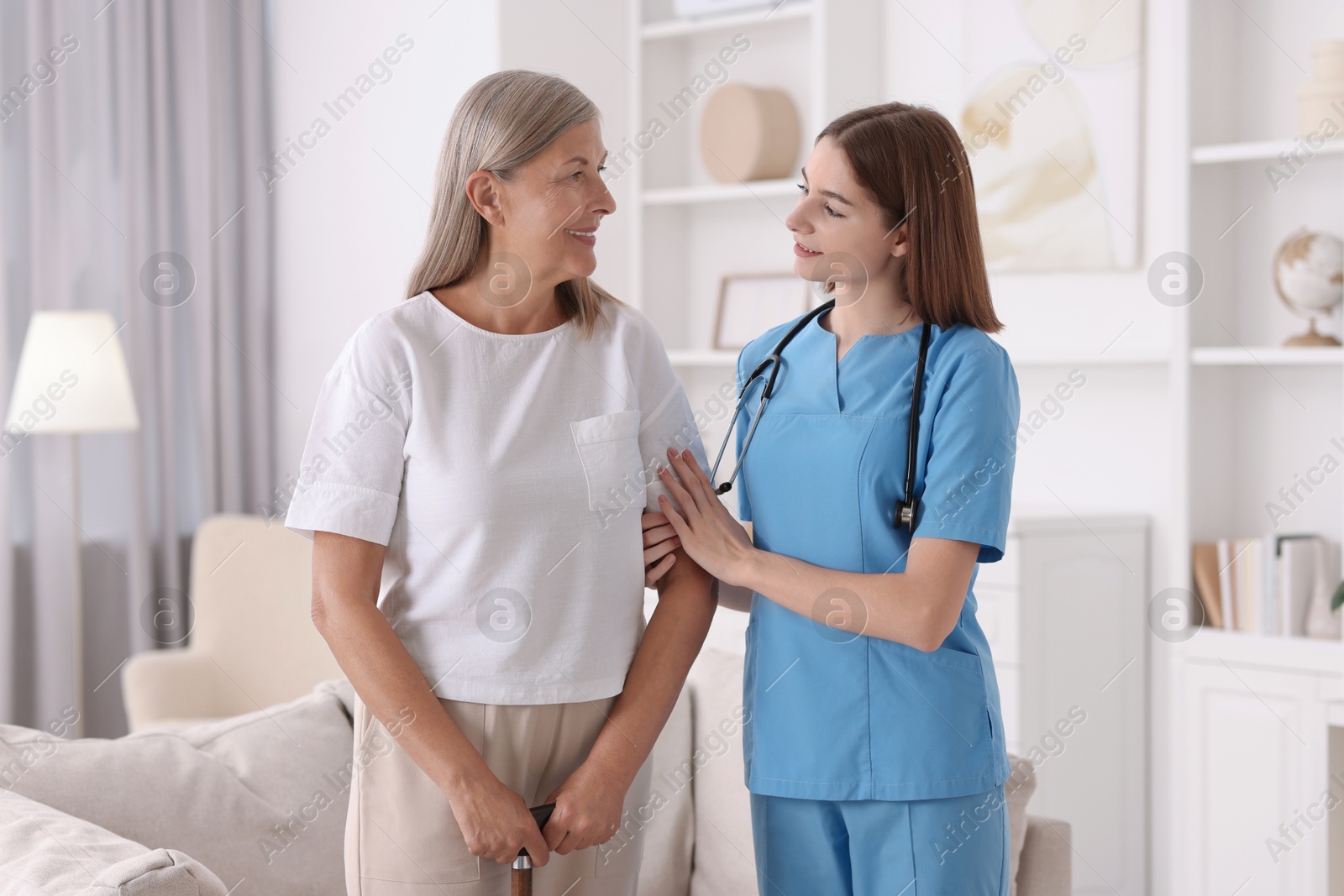 Photo of Young healthcare worker supporting senior patient indoors