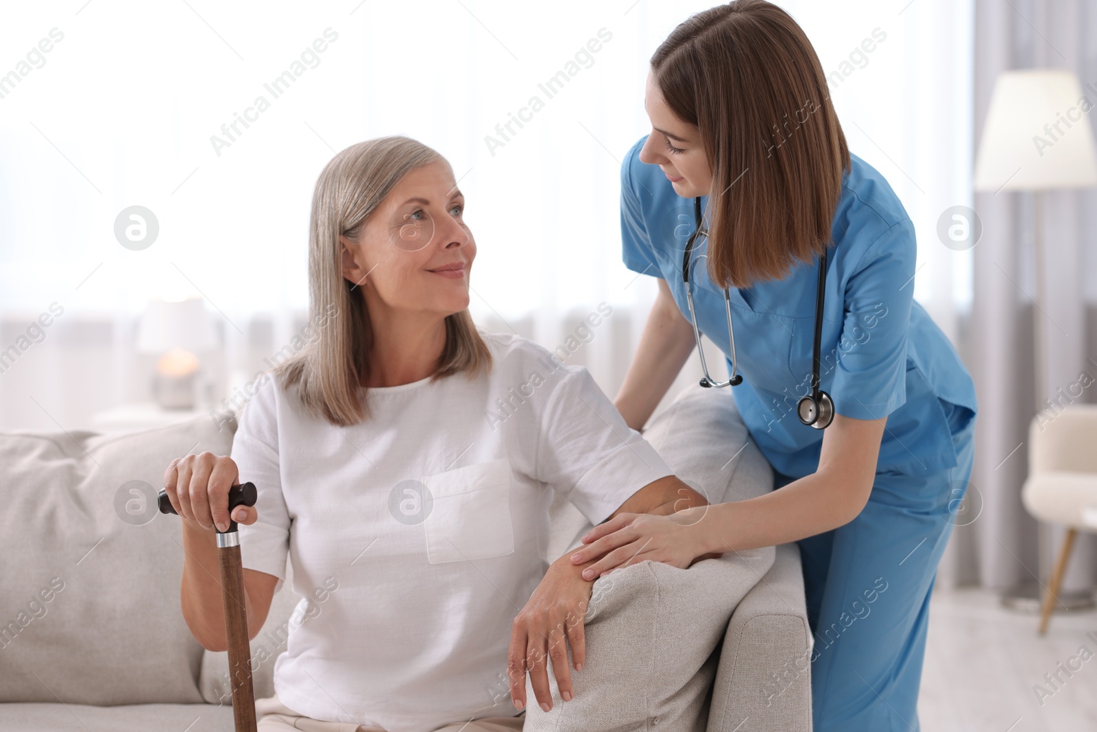 Photo of Young healthcare worker supporting senior patient indoors